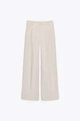 Pantalón de vestir color beige, de tiro alto y pernera ancha, con doble pliegue frontal, bolsillos laterales y de vivo en la espalda.