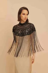 Capa corta negra con cuello alto y bordado de lentejuelas y mostacillas. Presenta flecos largos.