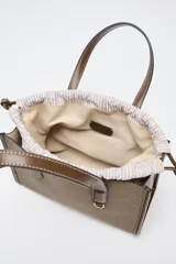 Bolso tipo shopper color marrón con doble asa corta y correa larga extraíble. Tiene detalle de pespuntes y anilla metálica decorativa. Incluye bolsa de tela interior extraíble con cierre fruncido.