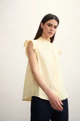 Camisa color amarillo pálido con cuello mao, sin mangas, con volados en los hombros y en el frente.