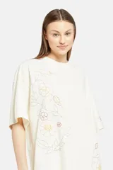 Remera color crema de corte holgado con cuello redondo y mangas cortas. Presenta un estampado floral en tonos beige y marrón a lo largo del frente y la manga derecha.