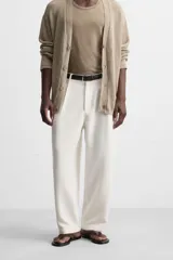 Pantalón blanco de corte relajado con pliegues frontales, bolsillos laterales y bolsillos traseros de vivo. Cierre frontal con cremallera y botón.