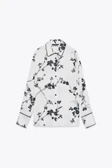 Camisa blanca con estampado floral negro, cuello solapa, manga larga y cierre frontal con botones.