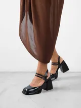 Zapato de tacón negro charol con plataforma, pulsera con dos tiras delanteras con cierre de hebilla y una trasera para sujeción en tobillo.