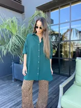 Camisa amplia de color verde, de manga larga y con un diseño curvo en el ruedo.