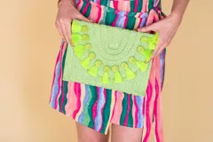 Sobre de ratán color naranja, con detalle de pompones y flecos a tono. Incluye correa para usar como cartera.