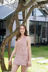 Vestido corto con lentejuelas rosadas, escote en V y breteles finos que se atan al cuello. Tiene corte a la altura de la cadera y falda con ruedo irregular.