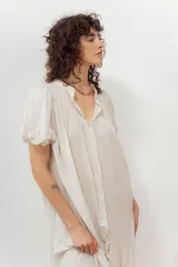 Vestido color beige con botones frontales, cuello camisero, mangas cortas abullonadas y falda con volantes.