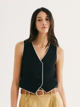 Chaleco negro con ribete blanco, cuello en V y cierre frontal con botones.