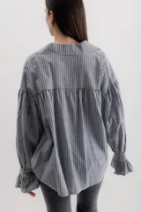 Camisa gris a rayas verticales blancas, de corte amplio, cuello alto con lazo y mangas largas abullonadas con puños elásticos.