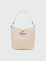Bolso tipo bucket XS de cuero color crema, con asa corta y correa larga extraíble. Cierre con broche metálico plateado.