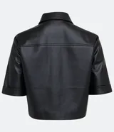 Camisa de manga corta confeccionada en material sintético color beige. Tiene cuello camisero, cierre de botones en forma de corazón, dos bolsillos con solapa y corte cropped.