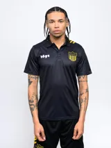 Remera polo negra de poliéster con cuello clásico, cierre de botones y mangas cortas. Presenta el escudo del Club Atlético Peñarol en el pecho, el número 1891 y detalles en amarillo en los hombros.