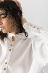 Camisa marrón de lino con cuello mao con volados, manga larga, cierre frontal con botones y bolsillo pequeño en el pecho.