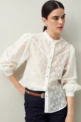 Camisa blanca con bordado floral en contraste, cuello mao, abotonadura frontal y mangas largas con frunces en los hombros.