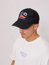 Gorra negra con visera curva y paneles traseros de malla. Presenta logo de la marca Rusty estampado en el frente en colores rojo, azul y gris.