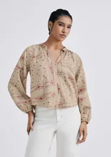 Blusa color beige con estampado de flores y líneas rojas, cuello con lazo y mangas largas abullonadas.