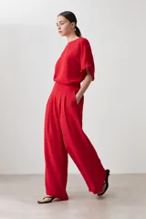 Pantalón palazzo rojo de tiro alto con pliegues marcados en la parte delantera y corte ancho y fluido. La modelo viste un conjunto monocromático con una blusa de manga corta a juego.