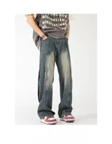 Pantalón de jean azul con efecto gastado y drapeados laterales que generan una abertura o pliegue vertical. Corte ancho y holgado.