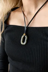 Collar con tiento de cuero negro y dije ovalado de piedra natural con patrón de manchas negras sobre fondo beige. Incluye un pequeño charm dorado con la palabra "AIRE" grabada.