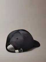 Gorra de béisbol negra con acabado satinado y visera curva. Presenta una placa metálica rectangular con el logo de Calvin Klein grabado en la parte frontal.