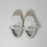 Zapatillas bajas de gamuza color beige y gris, con suela blanca y cordones gruesos blancos.