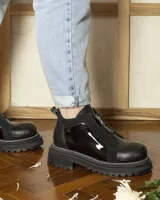 Botines de cuero negro con paneles laterales de charol, cierre frontal con cremallera y suela track.