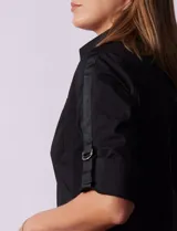 Camisa negra de algodón con cuello clásico, escote en V y mangas 3/4 con trabillas y lazos. Tiene dos bolsillos con solapa en el pecho y cierre frontal con botones.