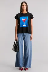 Remera negra de calce regular, confeccionada en jersey de algodón. Tiene cuello redondo, manga corta y estampado frontal de un trago con cereza sobre un fondo azul.