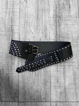 Cinto faja de cuero sintético negro con tachas plateadas y hebilla metálica dorada.