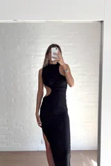 Vestido largo negro con cuello alto, sin mangas y abertura en la cintura.