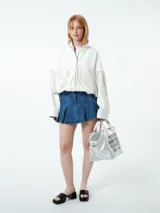Chaqueta blanca de cuero sintético con cuello camisero, cierre frontal con botones a presión y detalle de flecos en el pecho y las mangas.