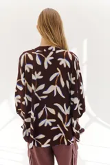 Camisa marrón con estampado de hojas blancas y azules, corte holgado, cuello mao, manga 3/4 y cierre frontal con botones.