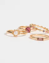 Set de cuatro anillos dorados con diferentes diseños: uno con una perla central, otro con una piedra rosa, otro con strass multicolor y otro con una piedra rectangular rosa.