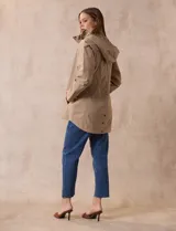 Campera impermeable color gris claro, marca Gallery. Tiene abertura central con cierre oculto y botones a presión, bolsillos delanteros y capucha plegable en el cuello.