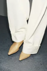 Botín de cuero color beige con punta fina y tacón kitten. Cierre con cremallera lateral.