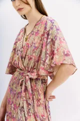 Vestido largo cruzado con estampado floral en tonos rosa, lila y dorado. Tiene mangas cortas amplias, escote en V y cintura elastizada con lazo.