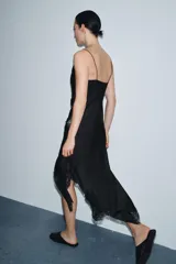 Vestido lencero de satén negro, corte midi asimétrico, con escote fluido y tirantes finos. Presenta drapeado lateral y aplicación de encaje a tono en el bajo.