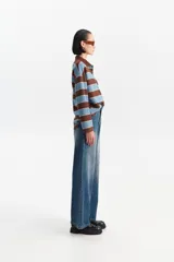 Jean de mezclilla azul con corte ancho y tiro medio, presentando un efecto desgastado en la parte frontal.