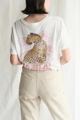 Remera de manga corta color blanco roto, con cuello redondo y un pequeño estampado frontal del logo de la banda Def Leppard en color rosado.