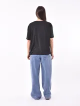 Remera negra de corte holgado con cuello en V y apliques de tachas doradas en los hombros.