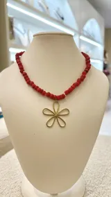 Collar corto de cuentas redondas de nácar rojo con dije de flor dorada.