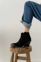 Bota corta de gamuza color marrón oscuro, con puntera cuadrada y detalles de costuras decorativas. Tiene un taco de madera con forma cónica.
