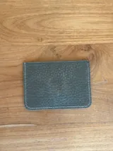 Tarjetero azul de cuero charol con tres ranuras para tarjetas y logo de la marca grabado en una placa dorada.