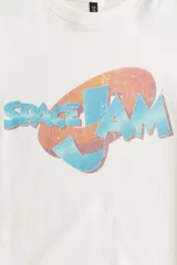 Remera color crema de algodón con estampado del logo de la película Space Jam en tonos celeste y naranja. Corte amplio con cuello redondo y mangas cortas.