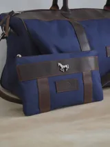 Sobre de lona azul con terminaciones en cuero marrón, logo de la marca Sierra Mora y aplique metálico de un caballo.