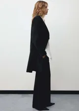 Abrigo negro de corte recto con doble botonadura, cuello con solapa de pico, bolsillos frontales con solapa y forro interior.