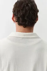 Camisa de manga corta color crema, de punto texturizado de mezcla de algodón de peso medio. Modelo con cuello abierto, tapeta lisa y bajo recto.