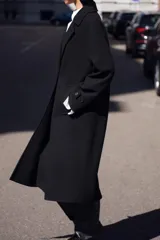 Abrigo negro de cuello solapa y manga larga con trabilla y botón. Tiene bolsillos delanteros de vivo y cierre frontal cruzado con botones.