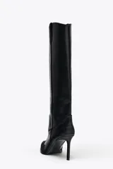 Bota alta de cuero sintético negro con detalles de pespuntes en contraste y puntera de gamuza. Tiene taco fino y tiradores laterales.